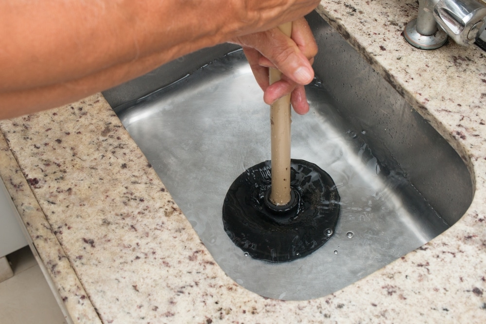 A person using a plunger to clear a drain.